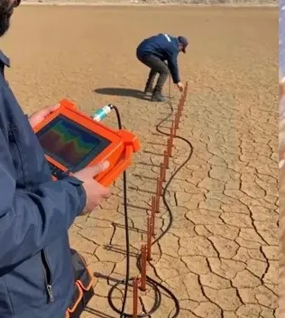 Prospection géophysique sur le terrain : l'opérateur lit les mesures sur l'appareil PQWT GT500A, les électrodes sont alignées le long du profil